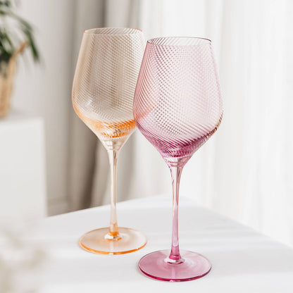 Two textured wine glasses, one orange and one pink, on a white surface with a light background.