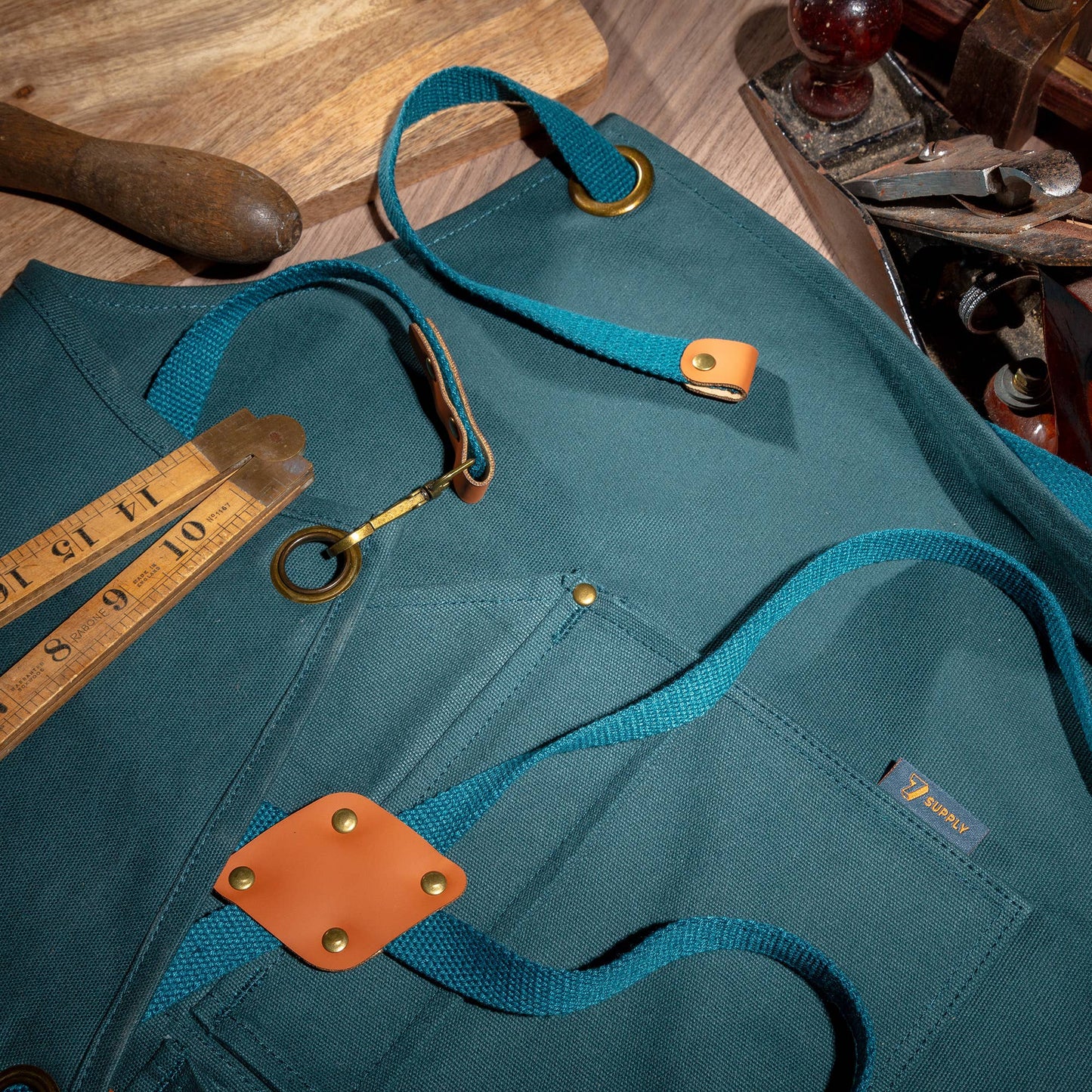 Teal apron with brown leather patches on a wooden surface with tools.