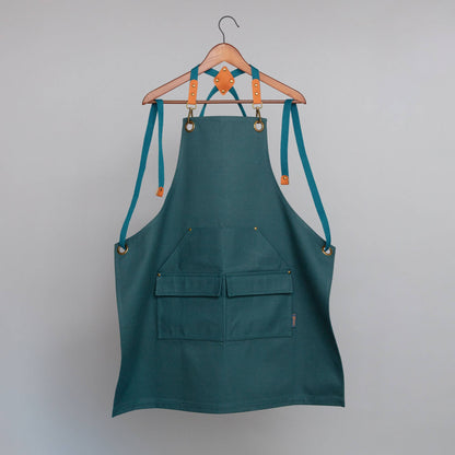 Green apron with teal straps hanging on a wooden hanger against a gray background