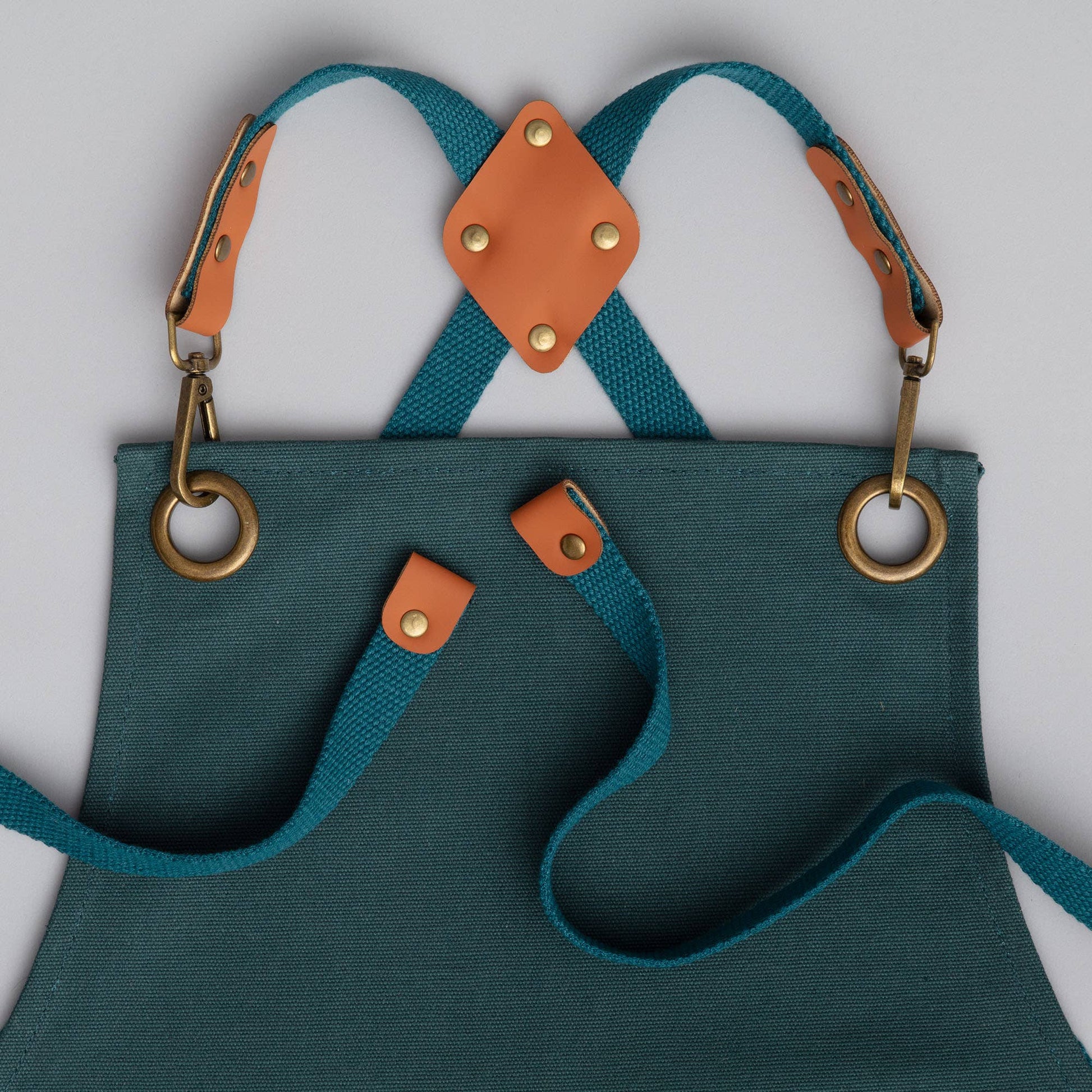 Teal apron with brown leather straps and accents on a light gray background