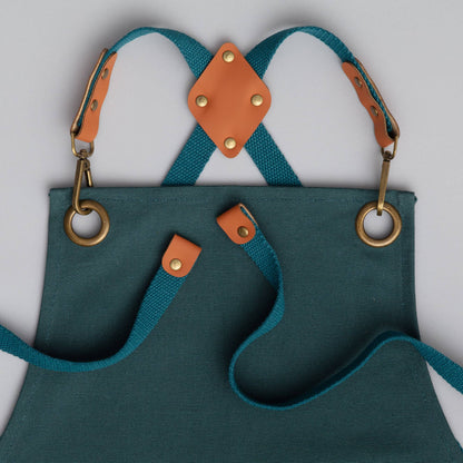 Teal apron with brown leather straps and accents on a light gray background