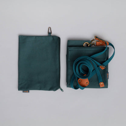 Green bag with strap and brown leather accents on a gray background