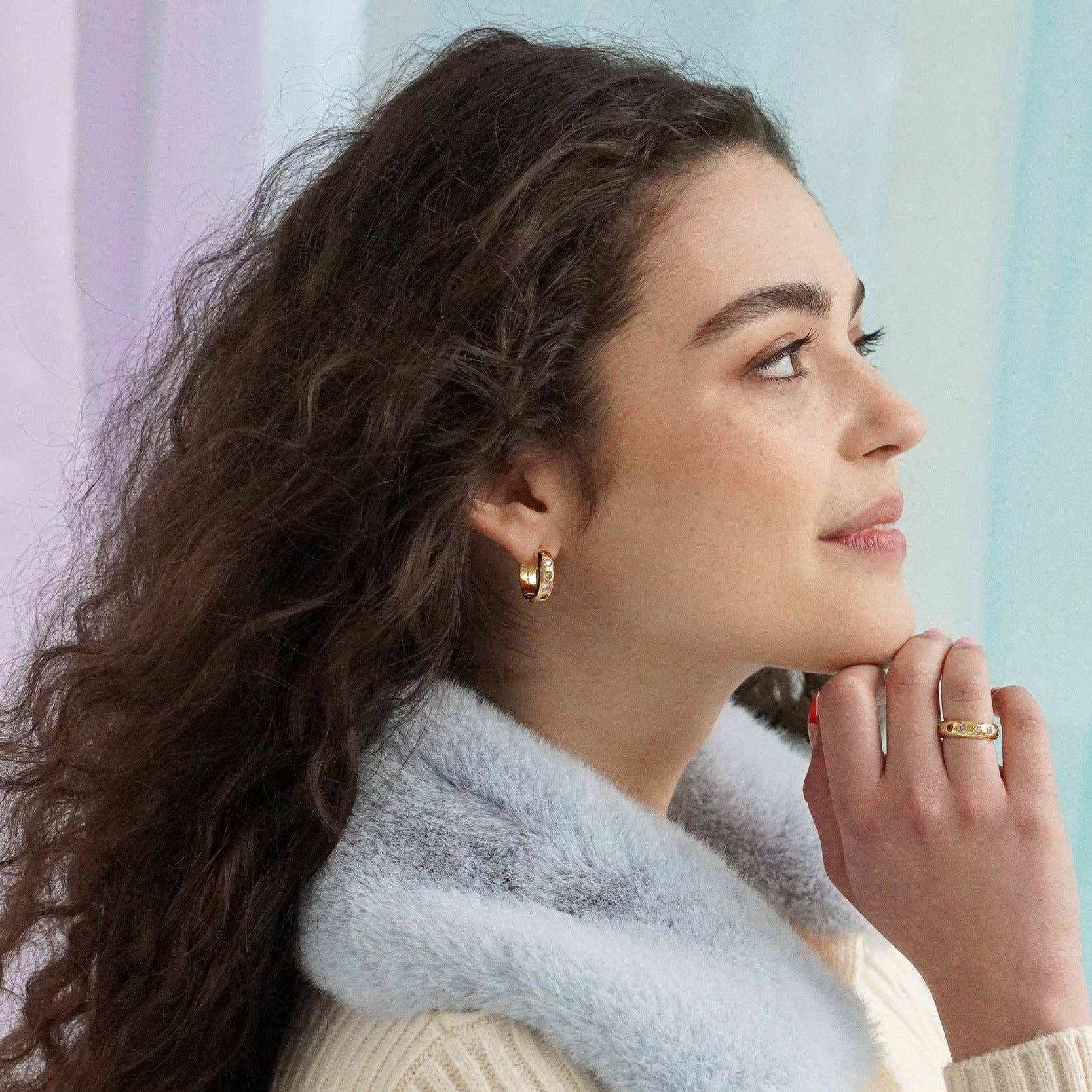 Woman wearing gold earrings and a ring, with a light blue background