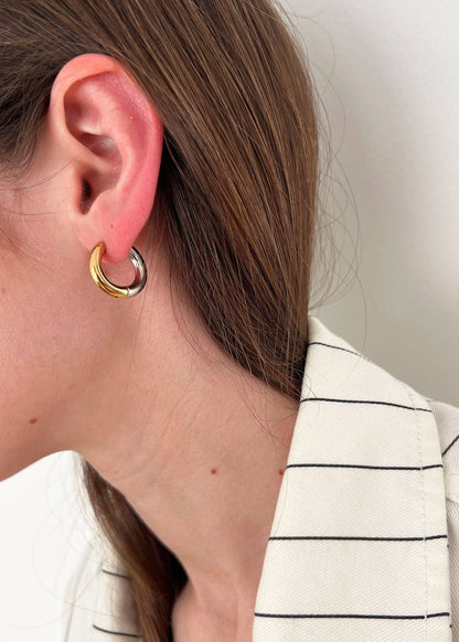 Close-up of an ear wearing a gold hoop earring with a neutral background