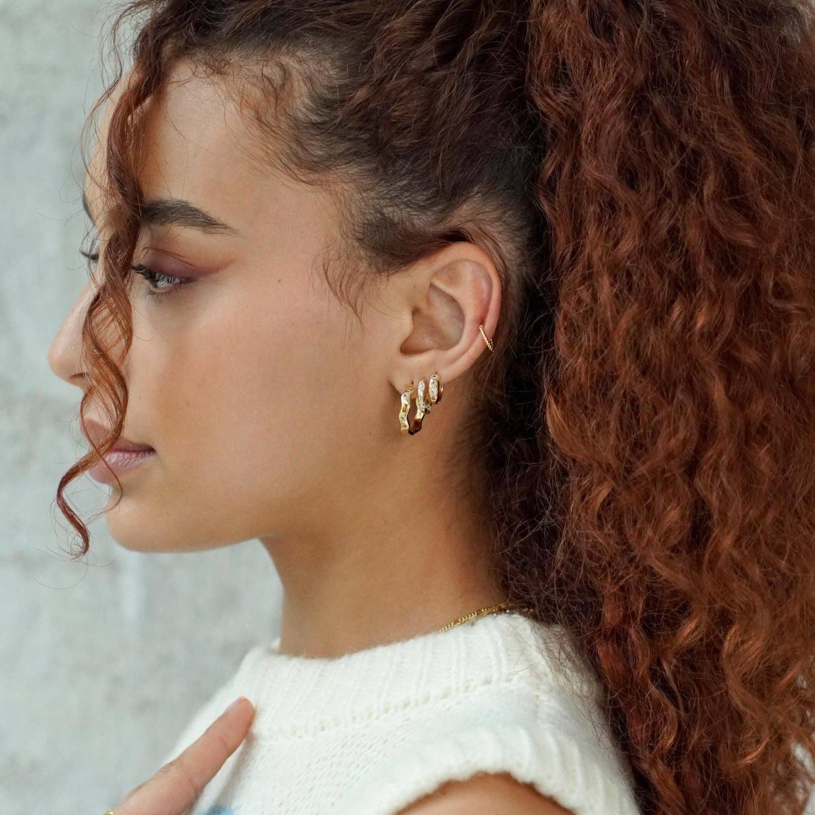 Close-up of a woman wearing gold hoop earrings with a neutral background