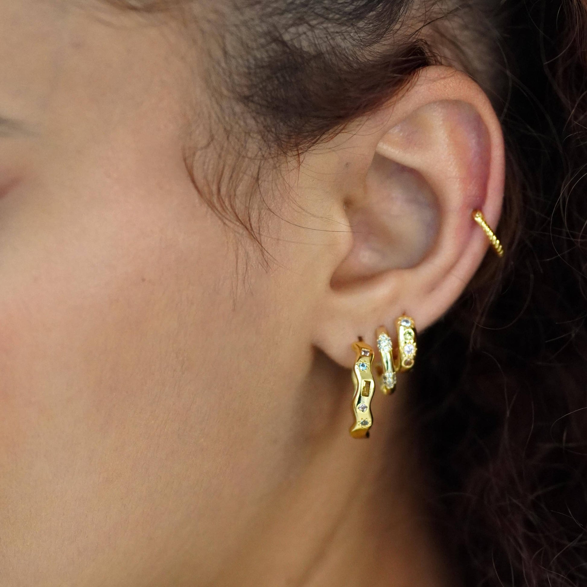 Close-up of an ear wearing gold hoop earrings with a blurred background