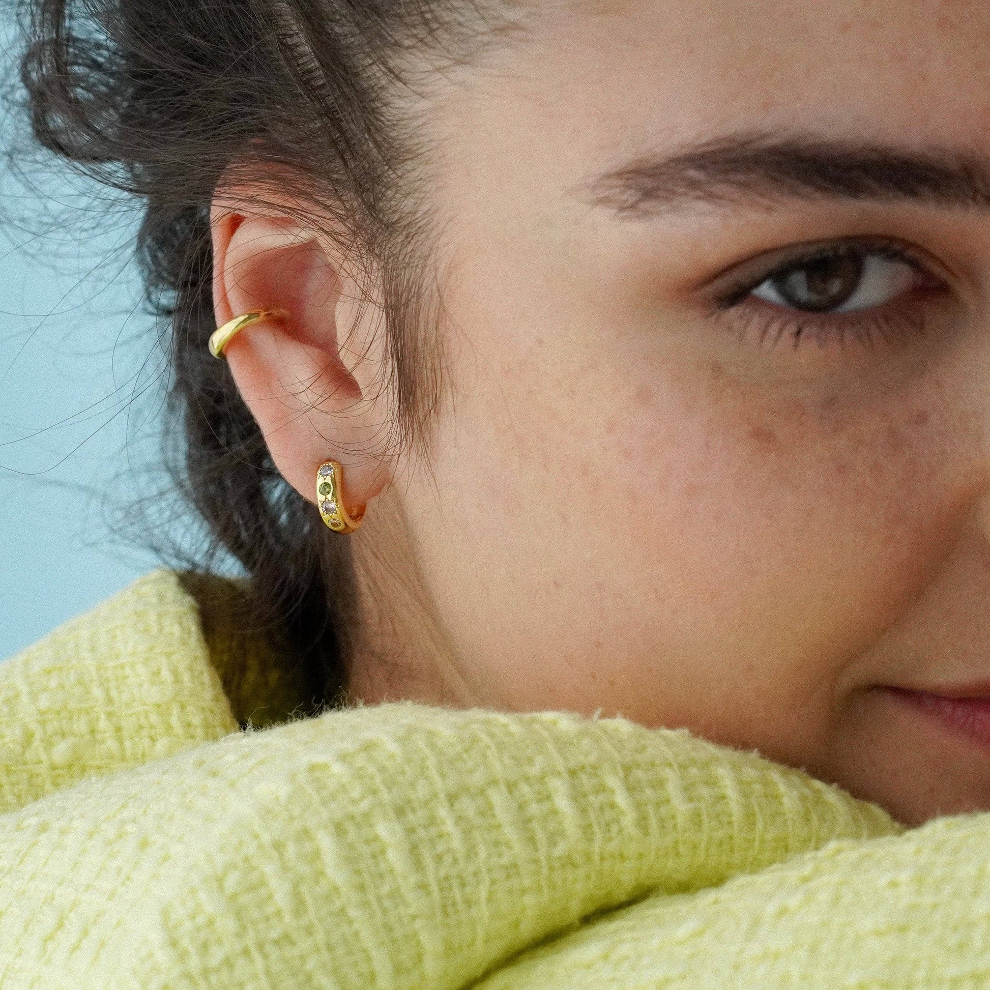Close-up of a person wearing gold earrings with a blurred background