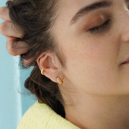 Close-up of a person wearing gold hoop earrings with a light blue background
