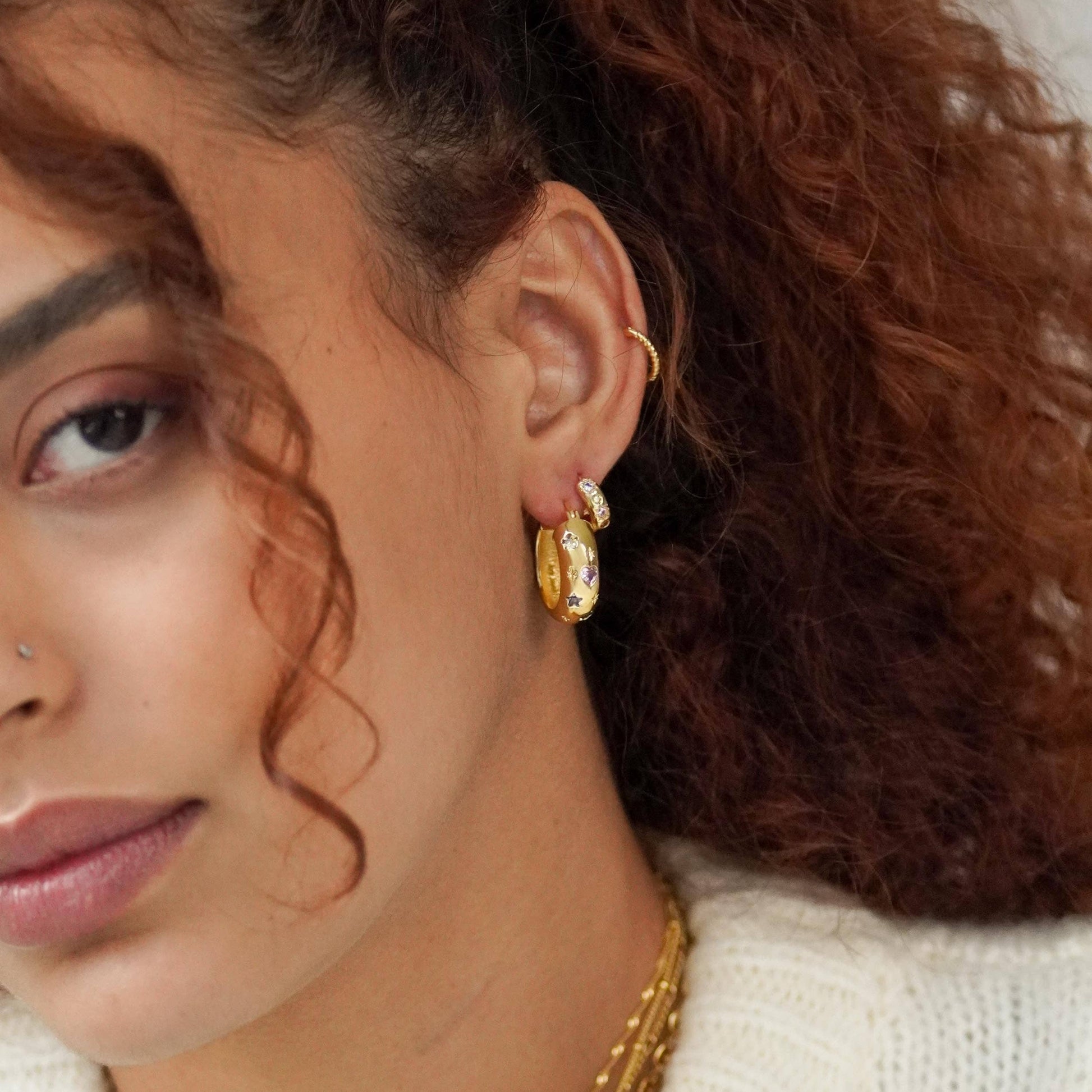 Close-up of a person wearing gold hoop earrings with a neutral background