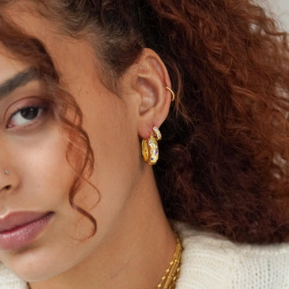 Close-up of a person wearing gold hoop earrings with a neutral background