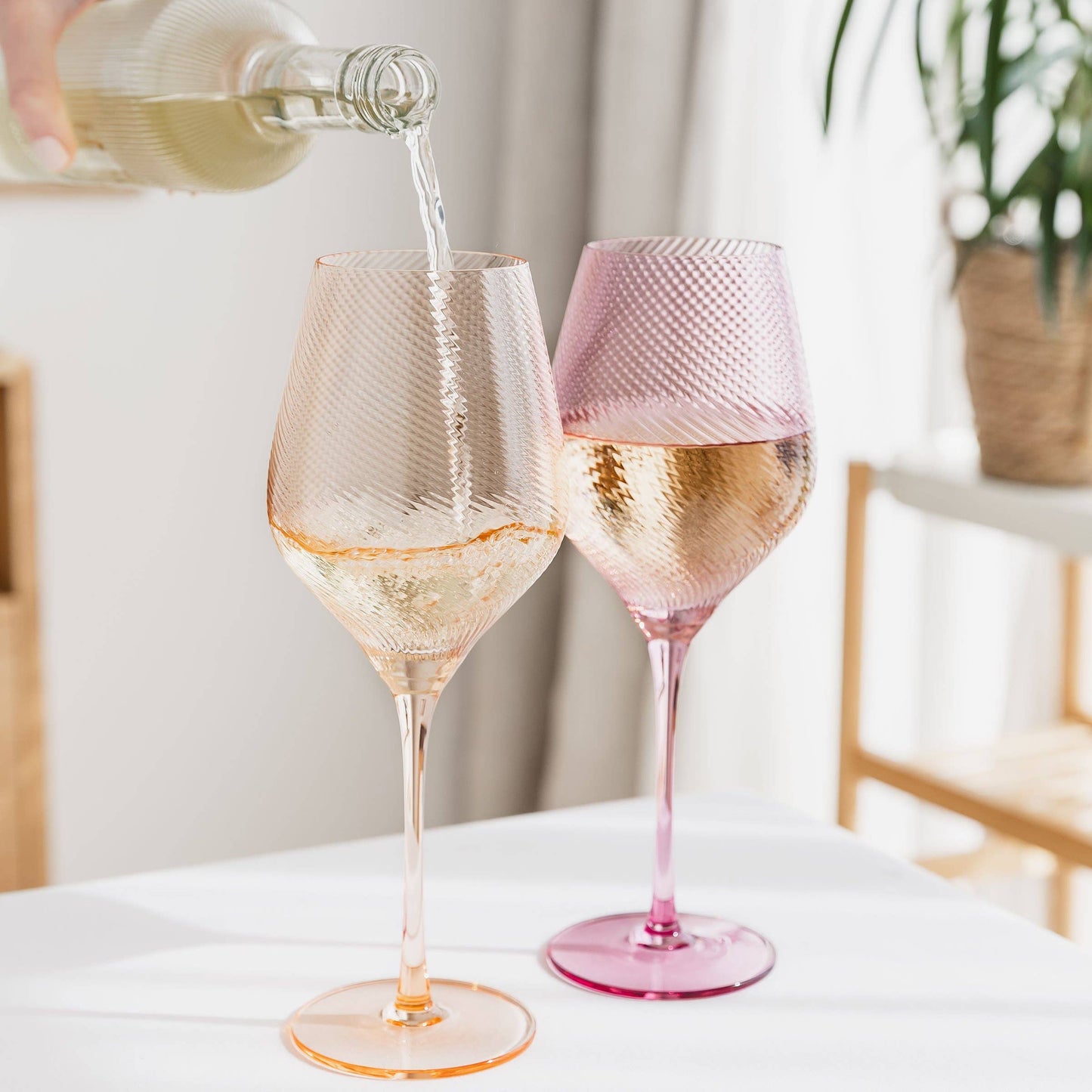 Two wine glasses being filled with a clear liquid on a white surface.