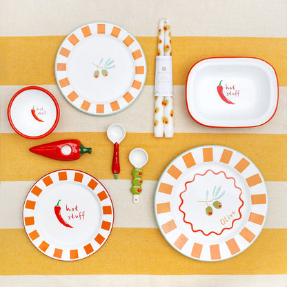 Set of children's plates, bowls, and cutlery with chili pepper design on a striped yellow and beige background.